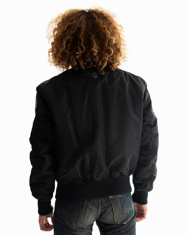 Rear view of a man with curly hair modeling the black Top Gun® MA-1 bomber jacket #color_black
