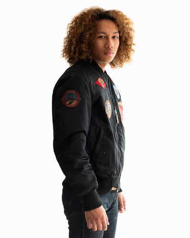 Man with curly hair modeling the black Top Gun® MA-1 bomber jacket from a different angle #color_black